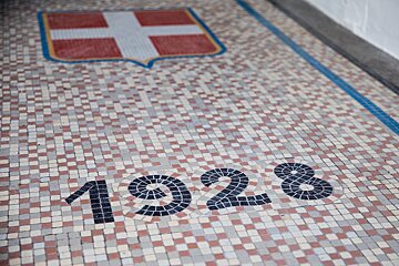 A mosaic floor features a red cross shield and the year 1928, all crafted from small, multi-colored square tiles.