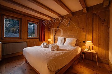 Cozy, rustic wooden bedroom with a large bed, ambient lighting, exposed beams, and forest views from windows, creating a chalet-style feel.