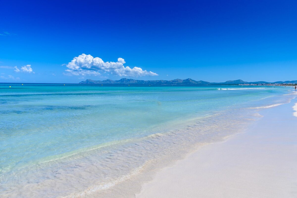 A beach with mountains in the background and a blue sky