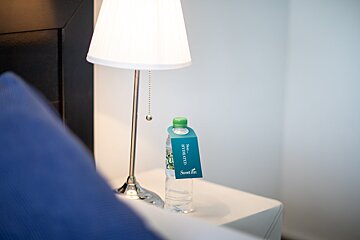 A bottle of water sits on a nightstand next to a lamp