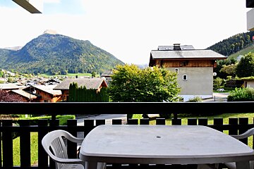View from a balcony with a plastic table and chairs, overlooking a scenic mountain landscape and chalets in a valley.