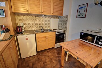 A compact kitchen featuring wooden cabinets, a tiled backsplash, sink, fridge, stove, microwave, and a wooden dining table.