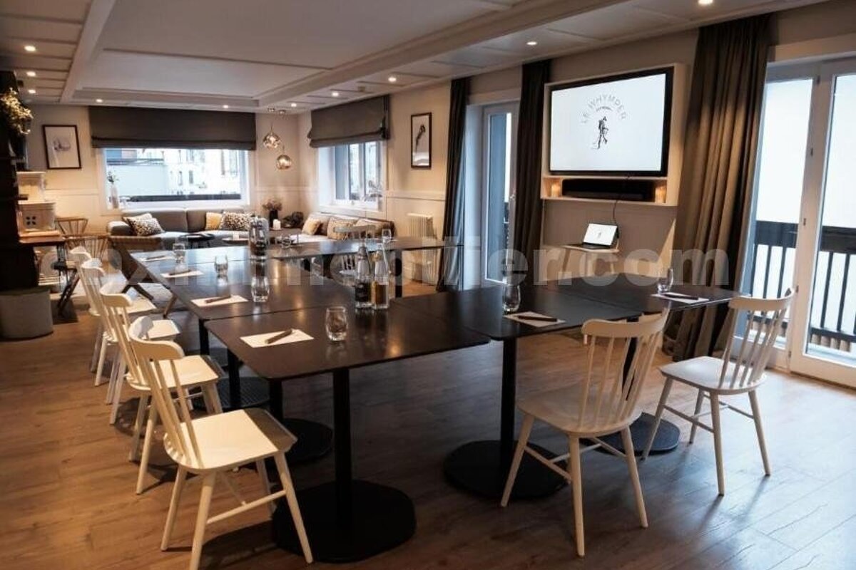 Stylish modern conference room featuring a large black table, white chairs, a TV display, and a comfortable lounge section by bright windows.