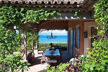 A beautiful Mediterranean-style outdoor living space with a vine-covered pergola, dining table, and breathtaking blue sea view.