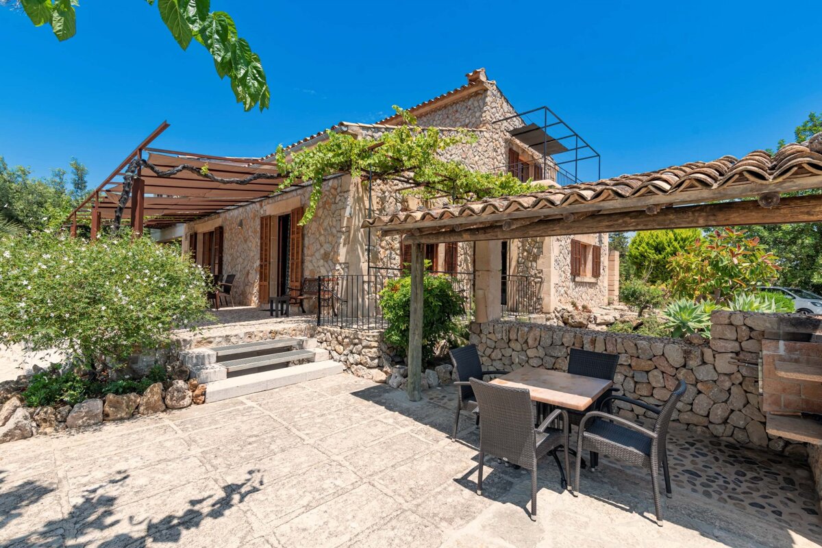 A stone house with a pergola and a table and chairs in front of it