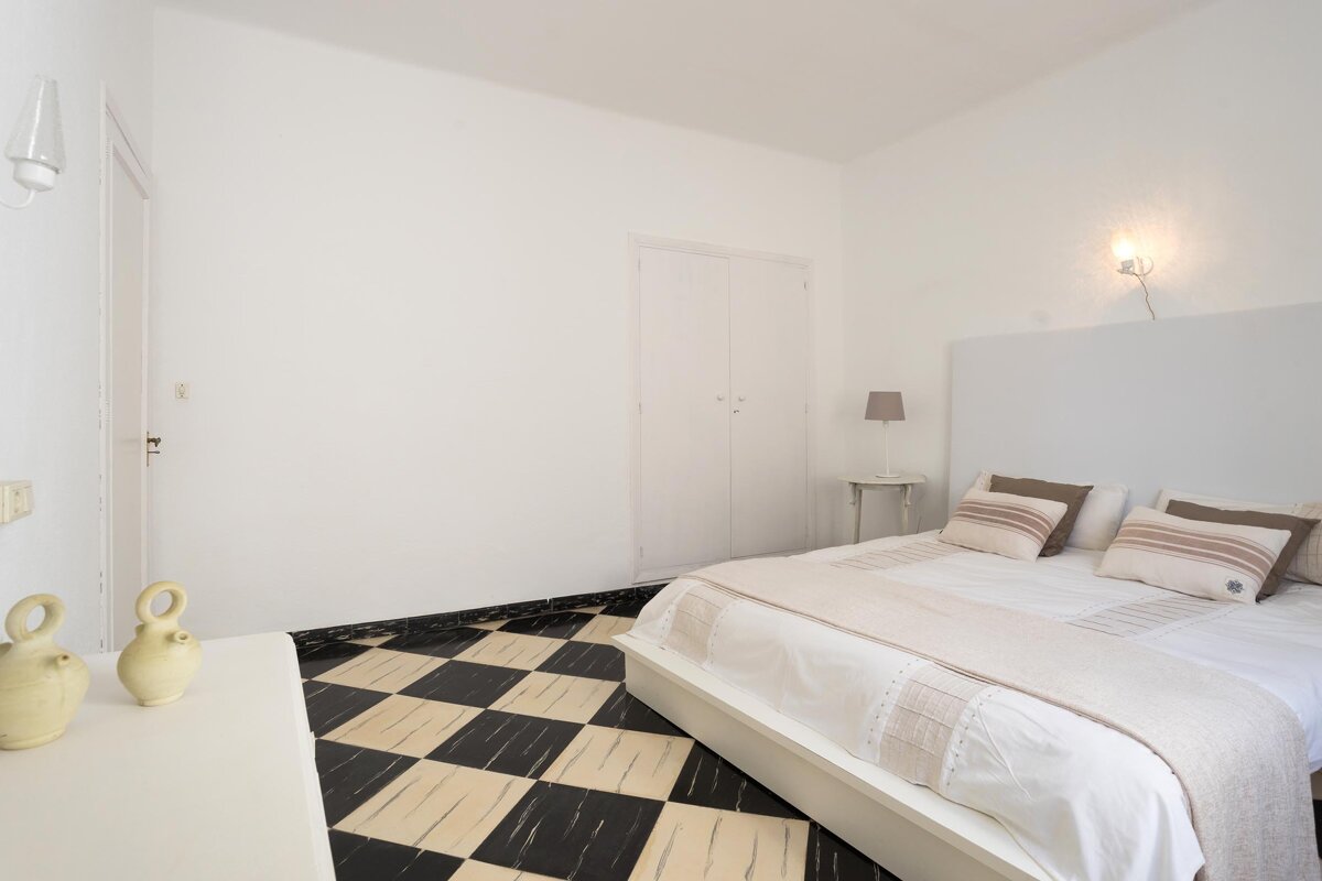 A bedroom with a checkered floor and a white bed