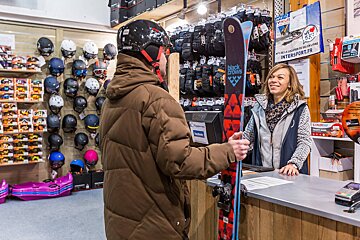 A man holding a skis in front of a sign that says intersport.fr