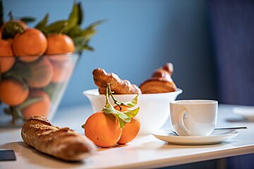 A bowl of oranges sits on a table next to a cup of coffee