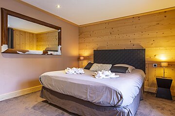 A cozy bedroom with a double bed, wood paneling, and a large mirror framed in cowhide on the wall.
