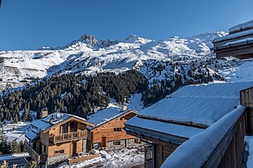 Snowy mountain village with traditional wooden chalets nestled against a backdrop of pine forests and majestic, snow-capped peaks under a clear blue sky.