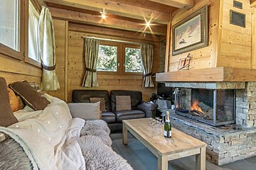 A bottle of champagne sits on a wooden table in front of a fireplace
