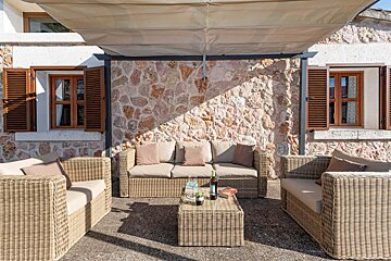 A patio with wicker furniture and a table with a bottle of wine on it