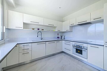 A sleek, modern white kitchen with U-shaped cabinetry, light countertops, integrated appliances, and minimalist design.