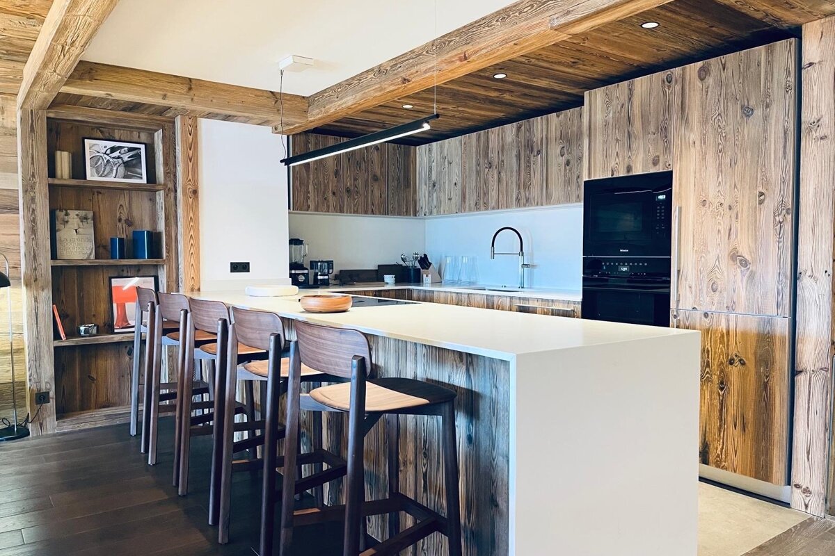 A stylish modern kitchen blending rustic distressed wood cabinets/ceiling with a sleek white island, bar stools, and integrated appliances.