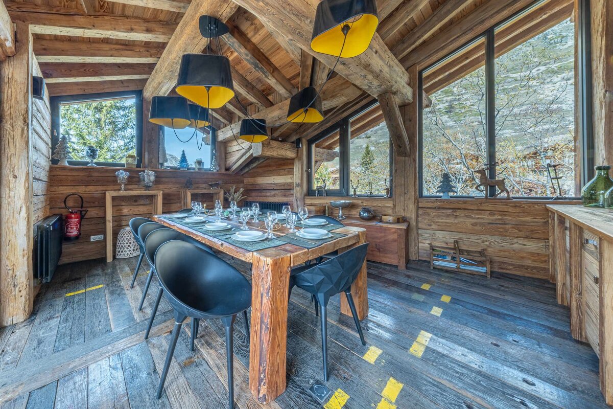 A rustic wooden chalet dining room featuring a set table, modern black chairs, and striking black-and-yellow pendant lights.