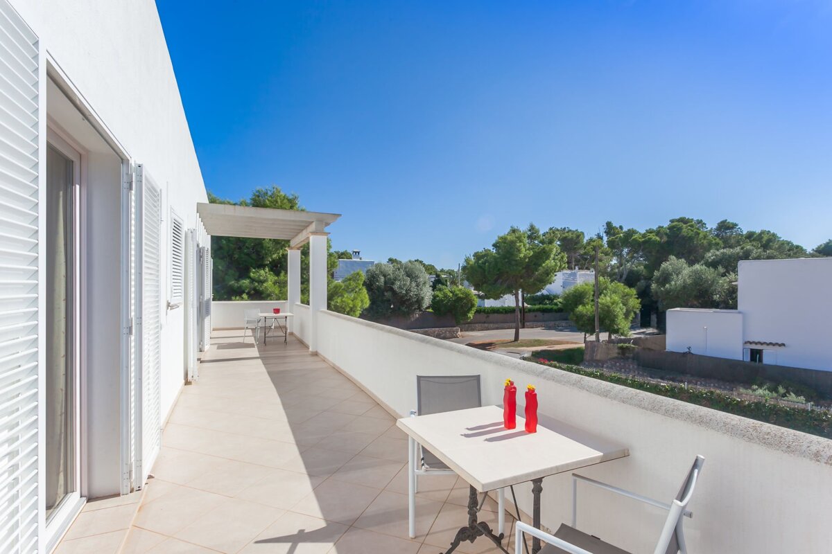A balcony with a table and chairs and two red vases on it
