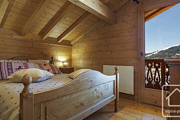 A bedroom in a wooden cabin with a bed and a balcony