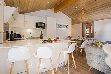 Modern chalet kitchen with white cabinets, a breakfast bar with three stools, and a warm, wooden vaulted ceiling.
