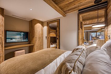 Warm chalet bedroom with wooden decor, TV, bunk beds seen through a doorway, and another room reflected in a large mirror.