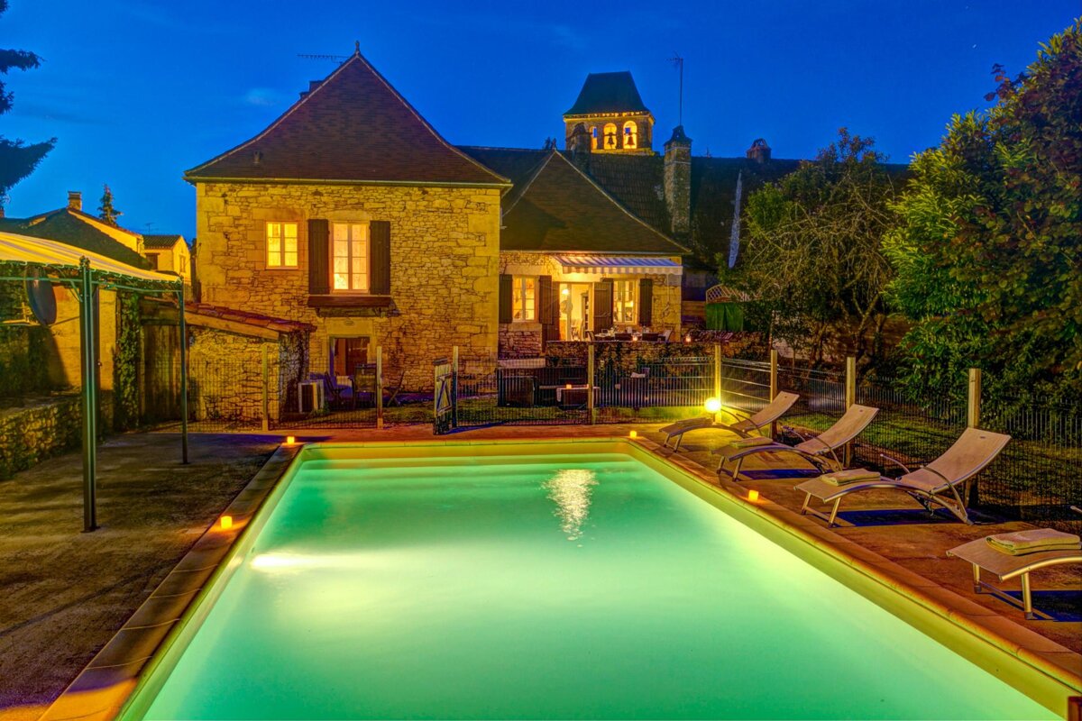 A large swimming pool in front of a house with a clock tower in the background