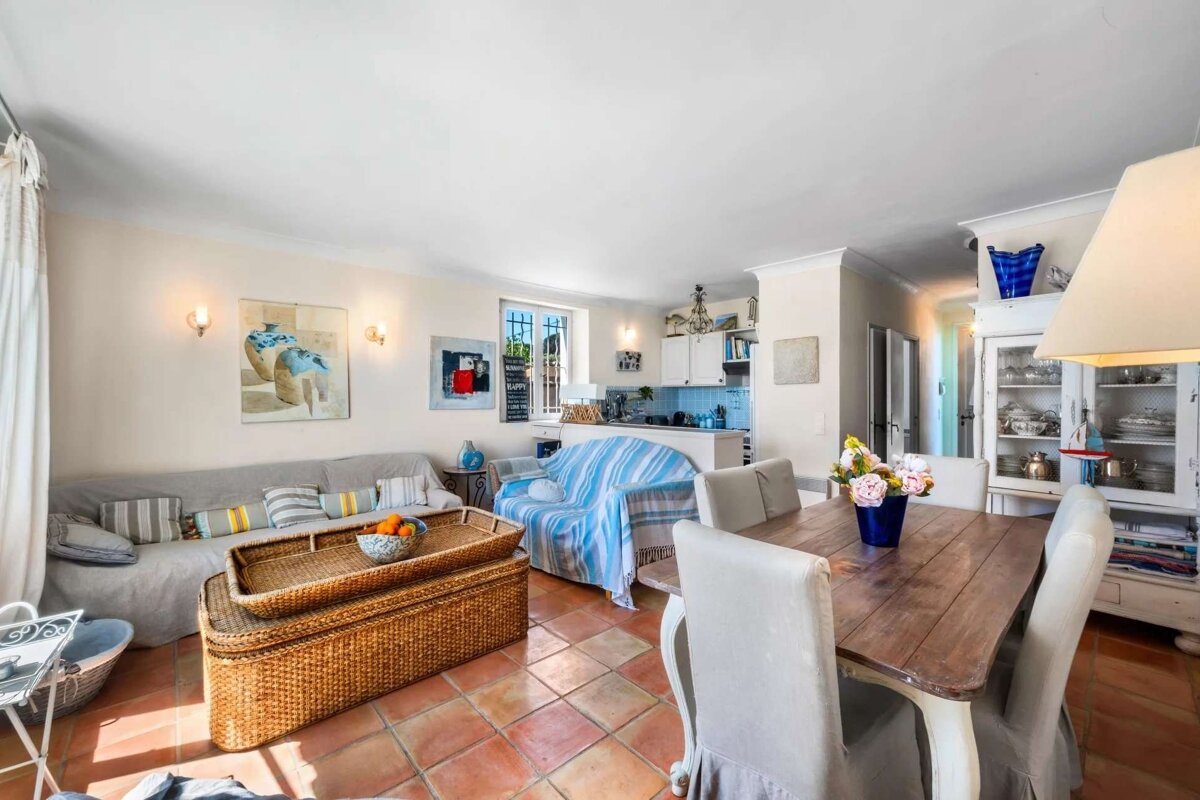 An inviting open-concept living, dining, and kitchen space with terracotta floors, comfortable sofas, and a rustic dining table.