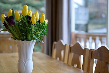 A white vase filled with yellow flowers sits on a table