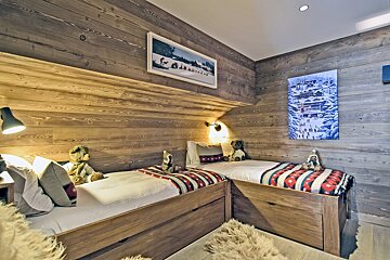 A cozy wooden cabin bedroom featuring two L-shaped beds decorated with teddy bears under rustic wood-paneled walls.