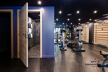 A sleek modern gym with fitness equipment next to an open door showing a tiled shower room.