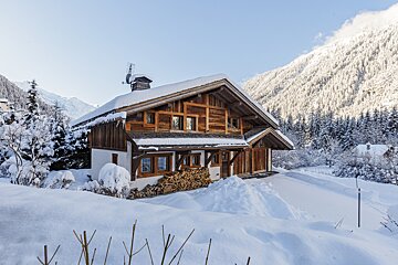 A snowy house with a pile of wood in front of it