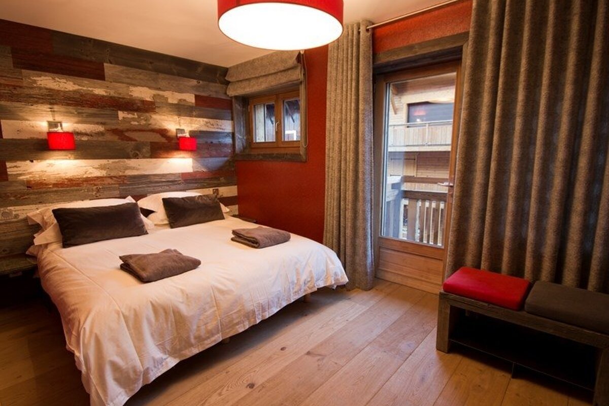 Cozy rustic bedroom with a reclaimed wood accent wall, a double bed with red sconces, and glass balcony doors.