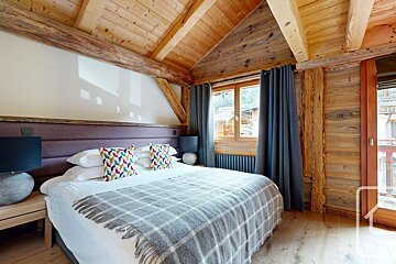 Rustic-modern bedroom with exposed wooden beams, a plush bed, a purple headboard, and colorful throw pillows.