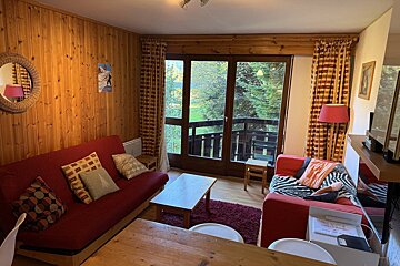 Cozy wood-paneled living room in a cabin, featuring red sofas, a wooden coffee table, and large glass doors opening to a balcony.