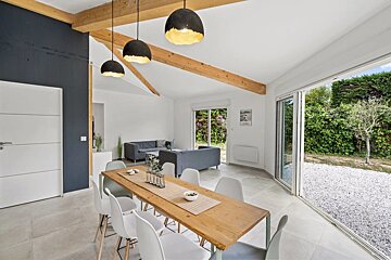 A modern dining area with a wooden table, hanging lamps, and large sliding doors opening to a yard.