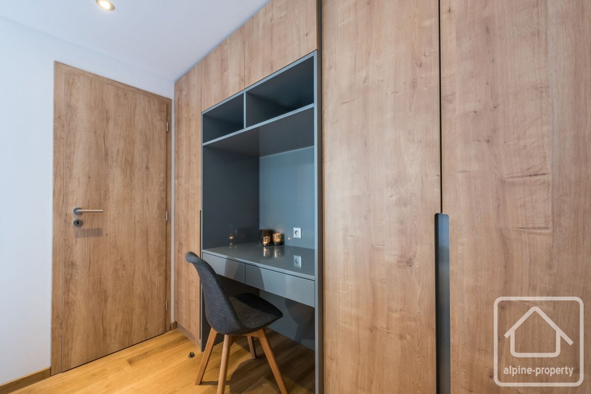 Modern room with wood-paneled walls. Features a built-in gray desk with shelving and a chair, next to a wooden door.