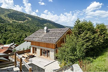 A house with a slate roof is surrounded by trees and mountains