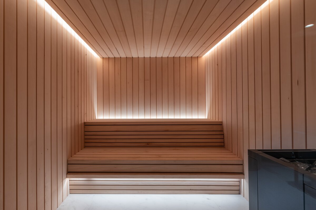 A minimalist wooden sauna featuring sleek paneling, tiered benches, and warm, indirect LED lighting.