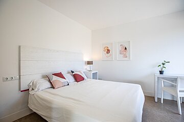 A bedroom with a bed and a desk with a plant on it