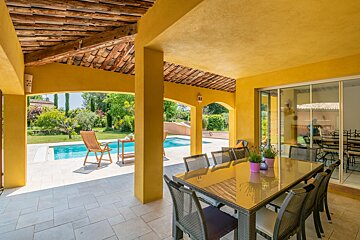 A patio with a table and chairs and a pool in the background