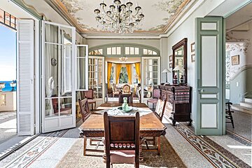 Grand dining room with a chandelier, ornate painted ceiling, mosaic floor, and French doors opening to both a sea-view balcony and an elegant sitting room.