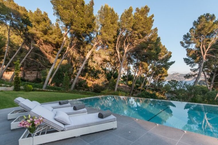 A swimming pool surrounded by trees with a view of the ocean