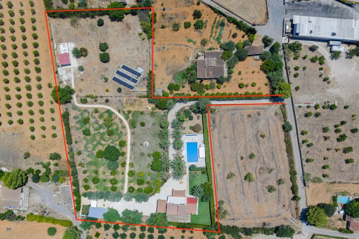 Aerial view of a large rural property featuring multiple buildings, a swimming pool, solar panels, agricultural fields, and roads, all outlined in red.