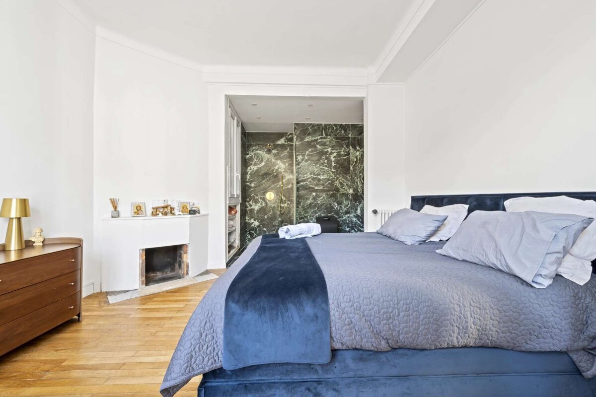 Modern bedroom with a blue bed, hardwood floor, corner fireplace, and a striking green marble shower in an adjacent alcove.