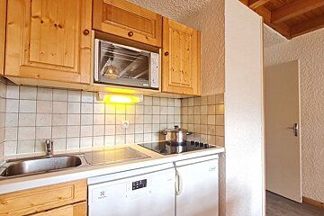 Cozy kitchenette featuring wooden cabinets, an integrated microwave, a stovetop with a pot, a sink, and white under-counter appliances.