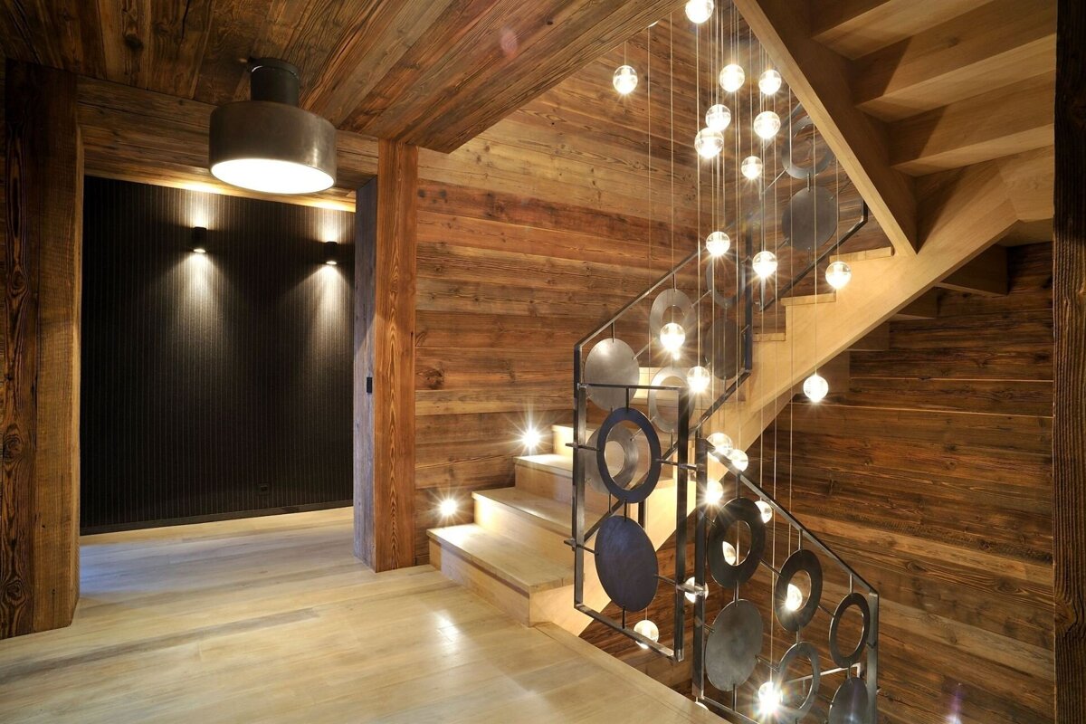 A wooden staircase with a metal railing and lights hanging from the ceiling