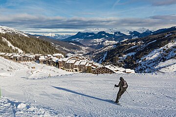 A person skiing down a snowy slope with mountains in the background