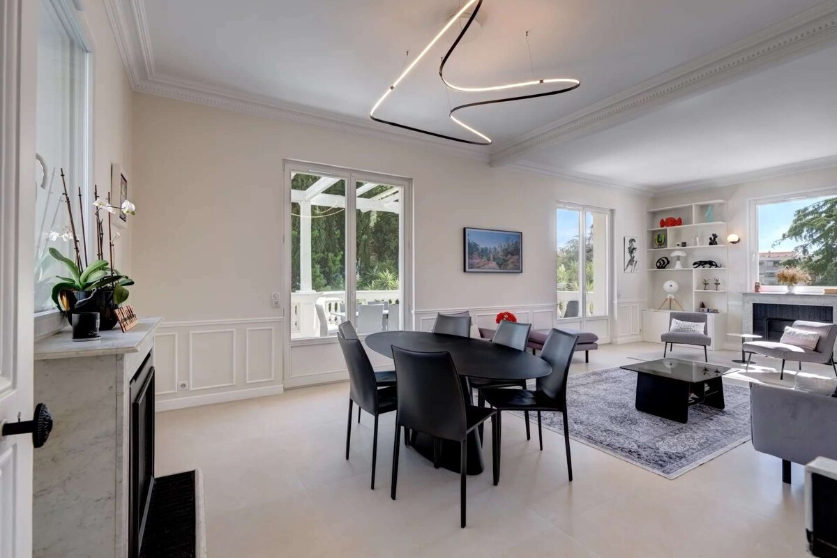A bright, modern open-plan living/dining room features a black dining set, a wavy ceiling light, white walls, and a living area with a fireplace.
