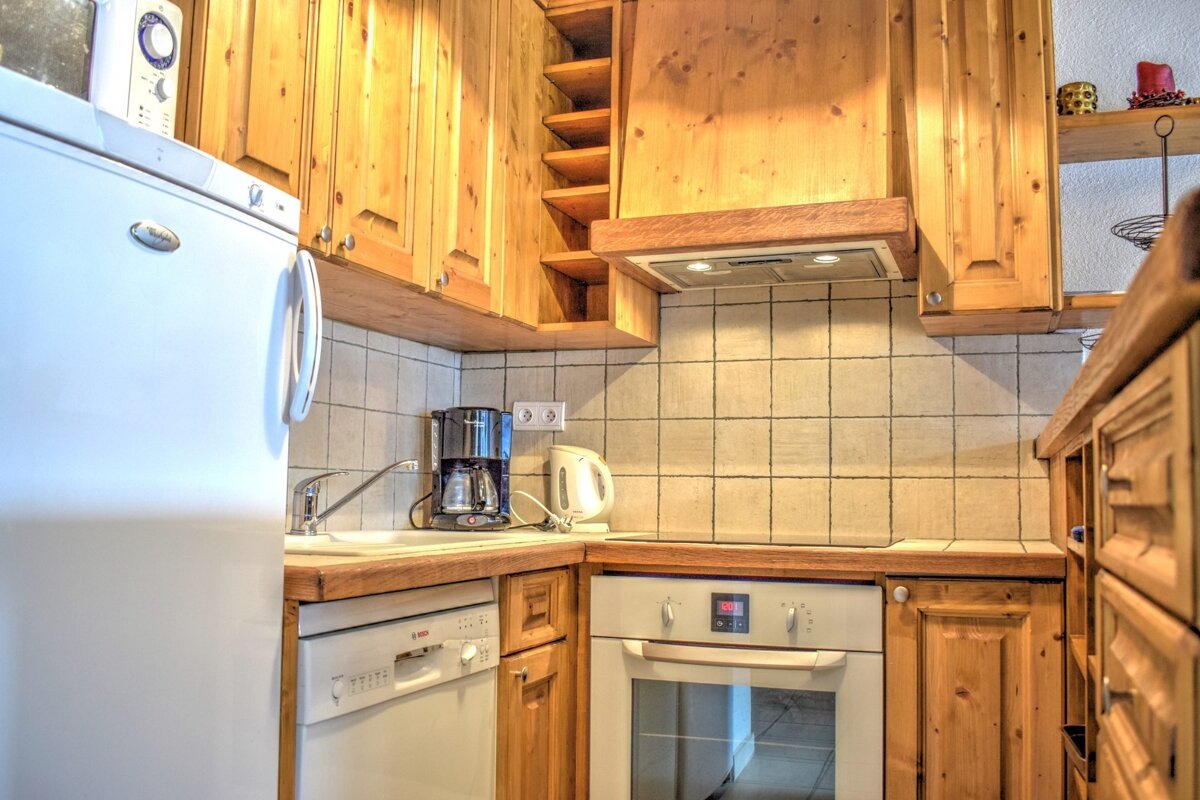 A cozy kitchen with knotty wood cabinets, white appliances, tile backsplash, and a coffee maker on the counter.