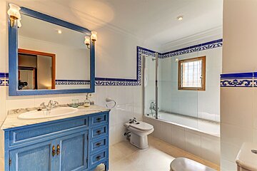 A blue and white tiled bathroom features a blue vanity, large mirror, bathtub with shower screen, bidet, and toilet.
