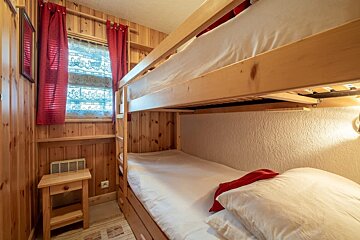 Small wood-paneled bedroom featuring a bunk bed with white bedding and a window with red curtains.