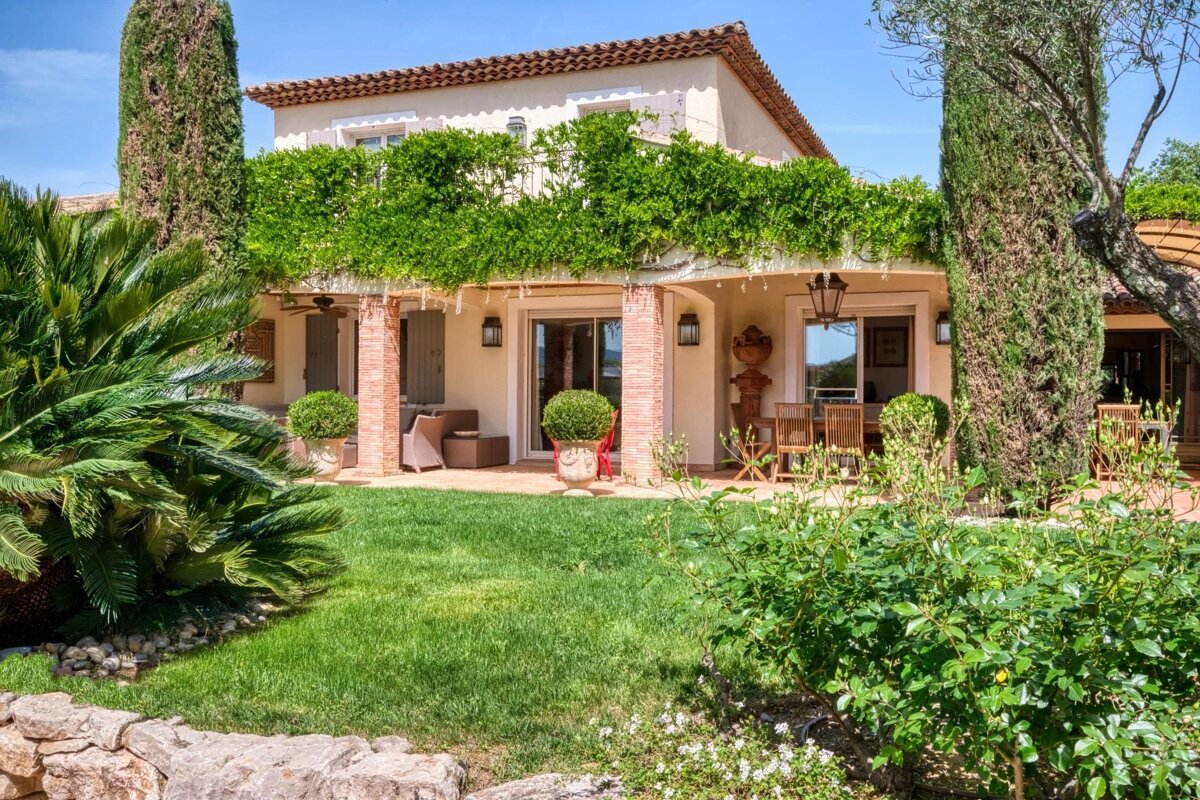 Beautiful Mediterranean villa with a terracotta roof, lush green vines draping the patio, and a neat lawn surrounded by gardens.
